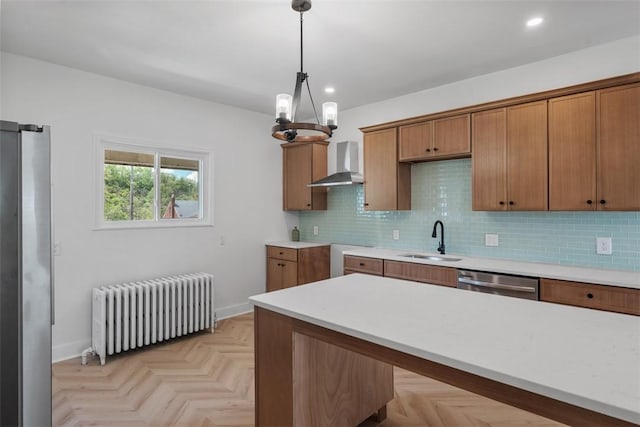 kitchen featuring radiator, a sink, dishwasher, wall chimney range hood, and decorative light fixtures