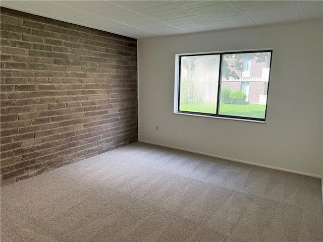 spare room featuring carpet, brick wall, and baseboards