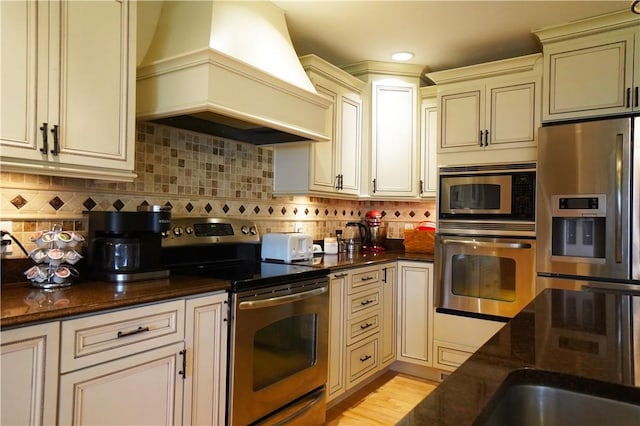 106 Arbor Trl, Slippery Rock Boro, PA 16057 - kitchen with stainless steel appliances, custom exhaust hood, cream cabinetry, dark stone countertops, and tasteful backsplash