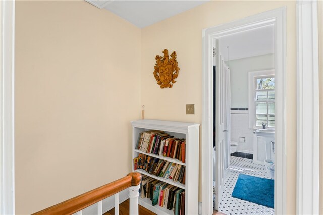 hall featuring tile walls, an upstairs landing, and wainscoting