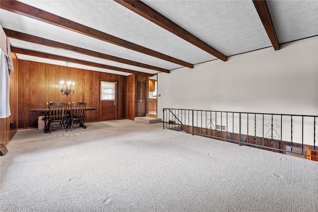 spare room featuring beamed ceiling, wooden walls, a chandelier, a textured ceiling, and carpet floors