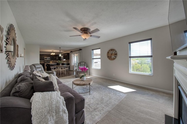 living area with a fireplace, light carpet, a ceiling fan, a textured ceiling, and baseboards