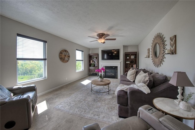 carpeted living room featuring a ceiling fan, a glass covered fireplace, baseboards, and a textured ceiling
