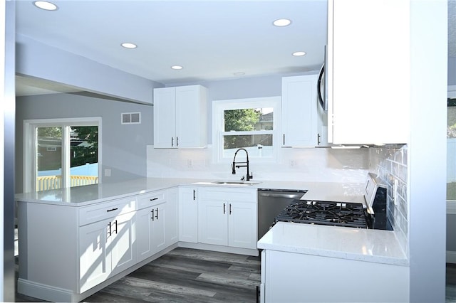 kitchen with a sink, a peninsula, dishwasher, stove, and white cabinets