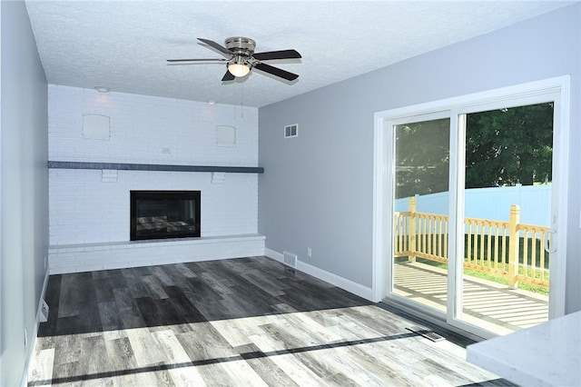unfurnished living room featuring a brick fireplace, a textured ceiling, wood finished floors, ceiling fan, and baseboards