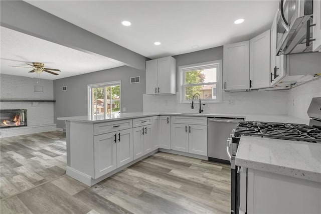 1301 Bechtel St, Monaca, PA 15061 - kitchen featuring appliances with stainless steel finishes, a peninsula, ceiling fan, light wood finished floors, and a brick fireplace