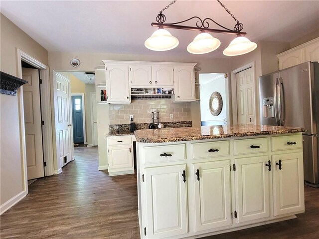 kitchen with stainless steel fridge, dark wood finished floors, dark stone counters, and a center island