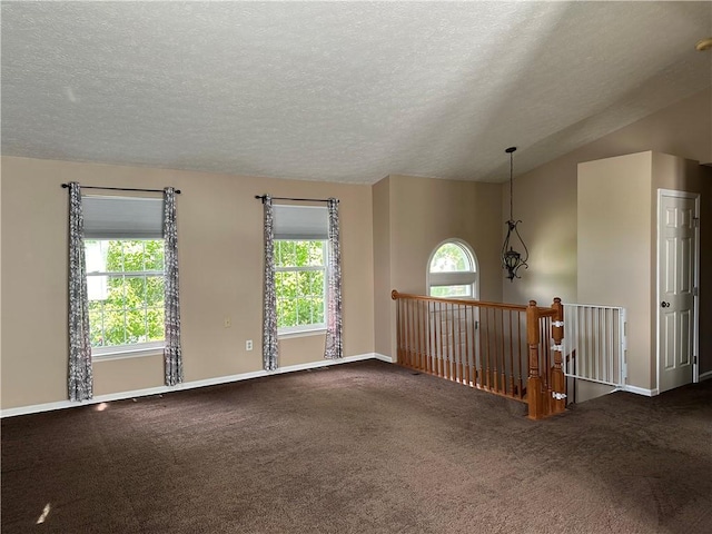 carpeted empty room with healthy amount of natural light, a textured ceiling, baseboards, and vaulted ceiling