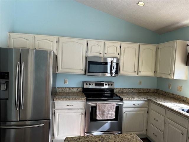 kitchen featuring stainless steel appliances, lofted ceiling, a textured ceiling, and white cabinets