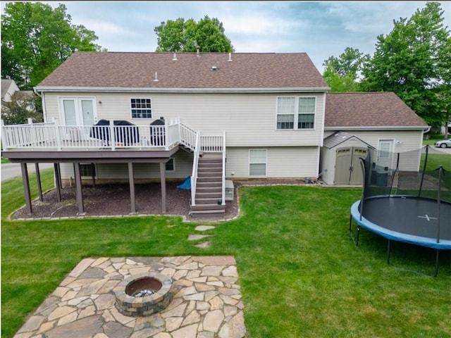 rear view of property with a trampoline, stairway, a fire pit, a shed, and a deck