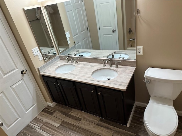 bathroom with toilet, double vanity, baseboards, and wood tiled floors