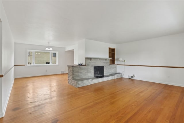 unfurnished living room featuring a chandelier, light wood-type flooring, a fireplace, and baseboards