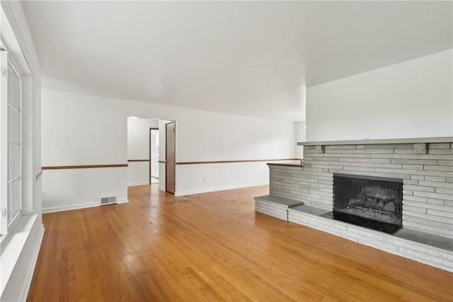 unfurnished living room with a stone fireplace, wood finished floors, and baseboards