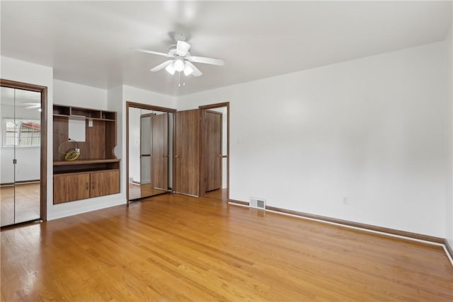 unfurnished bedroom featuring light wood-style flooring, two closets, baseboards, and a ceiling fan