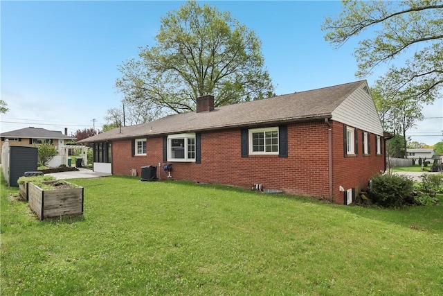 rear view of property with brick siding, a chimney, a yard, and central AC unit