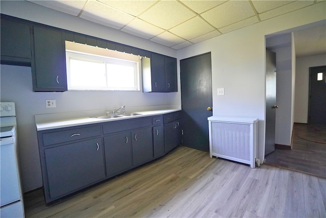 kitchen with a sink, radiator heating unit, white range with electric cooktop, light wood-style flooring, and a paneled ceiling