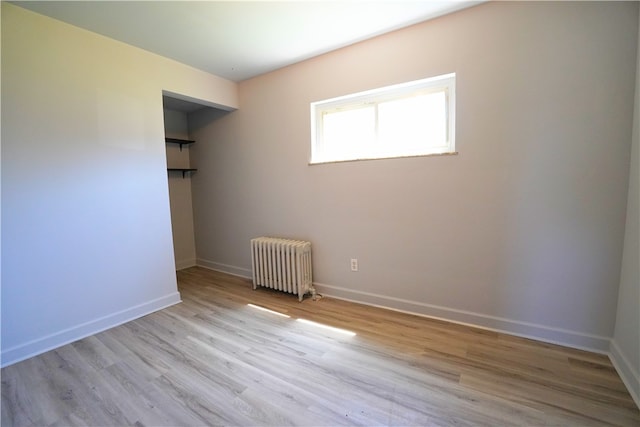 unfurnished room featuring radiator heating unit, light wood-style floors, and baseboards