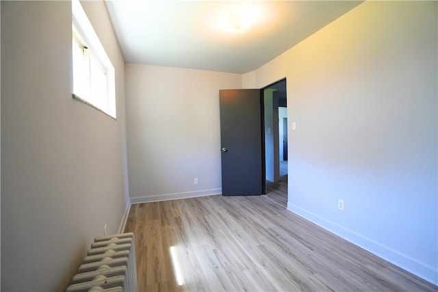 unfurnished room with radiator heating unit, wood finished floors, and baseboards