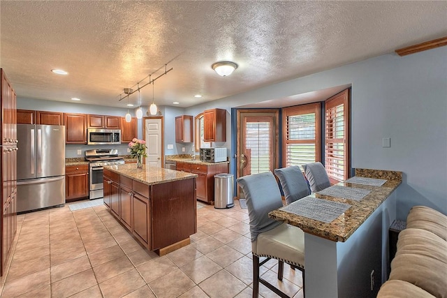 1057 Finchley Rd, North Huntingdon, PA 15642 - kitchen featuring stainless steel appliances, a textured ceiling, brown cabinets, a kitchen island, and light stone counters