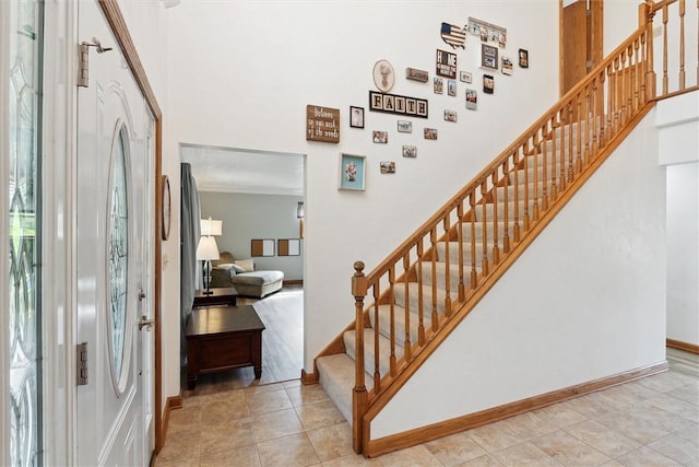 foyer entrance featuring a towering ceiling, stairs, baseboards, and tile patterned flooring