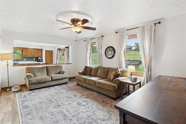 living area with light wood-style floors, a ceiling fan, and baseboards