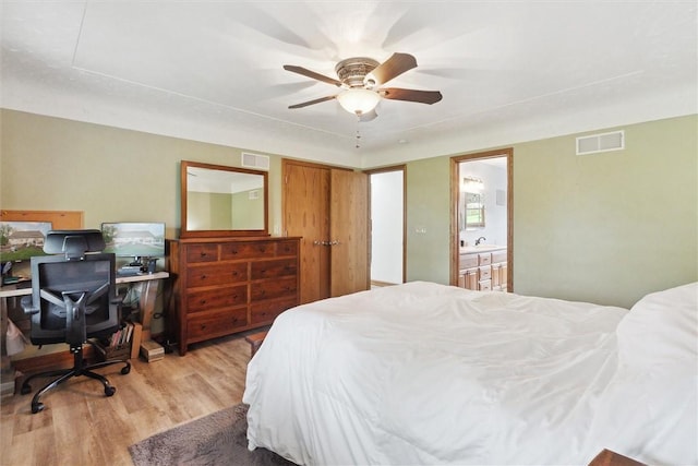 bedroom featuring light wood-type flooring, ensuite bath, an office area, ceiling fan, and a sink
