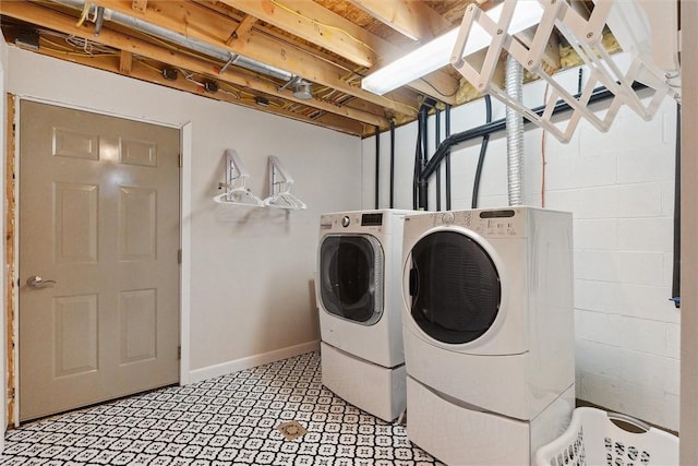 clothes washing area featuring washing machine and dryer, baseboards, and concrete block wall