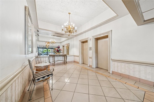 corridor featuring a chandelier, light tile patterned floors, wainscoting, a textured ceiling, and a raised ceiling