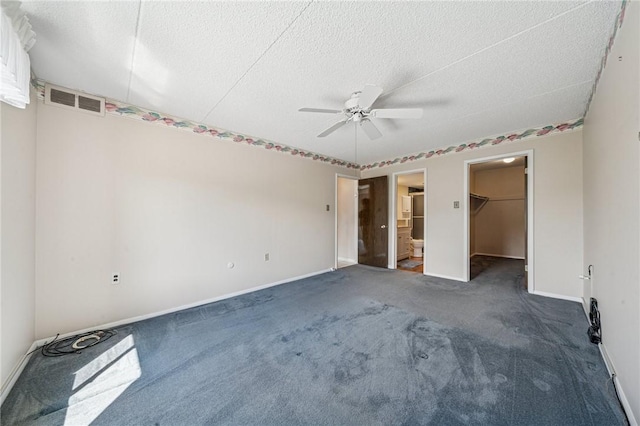 unfurnished bedroom with carpet flooring, a walk in closet, baseboards, a textured ceiling, and ceiling fan