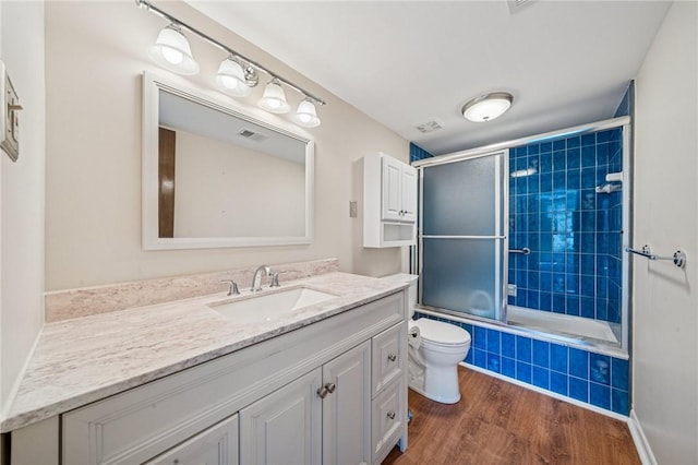full bathroom with wood finished floors, vanity, tiled shower / bath combo, and toilet