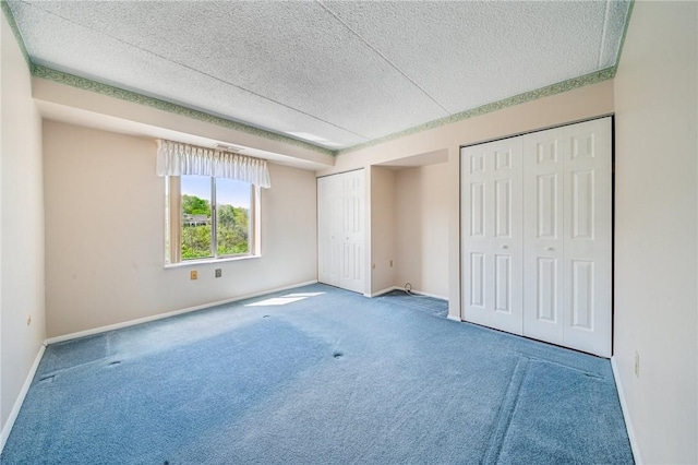 unfurnished bedroom with two closets, a textured ceiling, carpet flooring, and baseboards