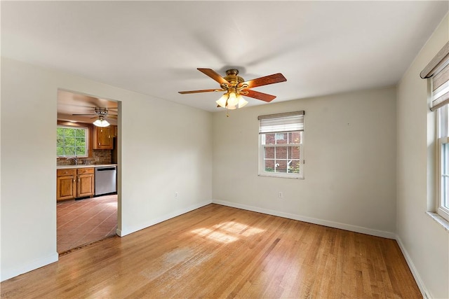 spare room with light wood finished floors, a sink, ceiling fan, and baseboards