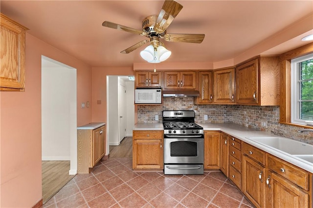 kitchen with stainless steel gas stove, white microwave, light countertops, backsplash, and a sink