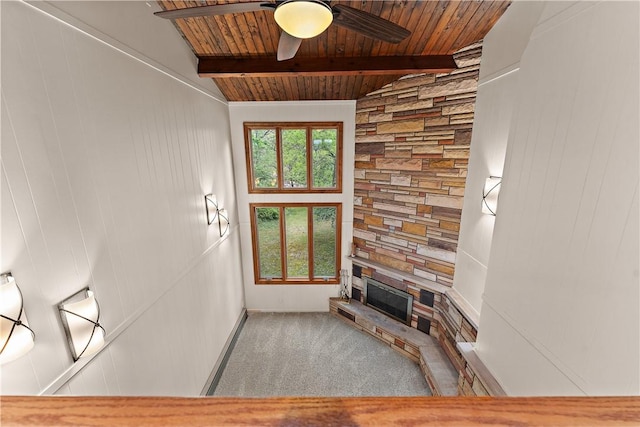 unfurnished living room with wood ceiling, beam ceiling, a stone fireplace, ceiling fan, and carpet