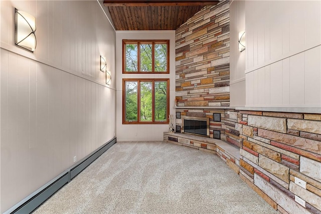 unfurnished living room featuring a baseboard radiator, carpet flooring, wood ceiling, a stone fireplace, and a high ceiling