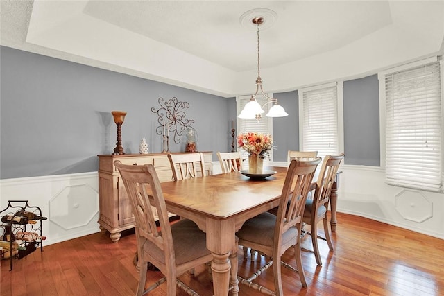 dining room featuring a tray ceiling, dark wood-style floors, a wainscoted wall, and a chandelier