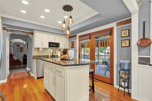 kitchen with black microwave, dishwasher, arched walkways, a kitchen breakfast bar, and light wood-style flooring