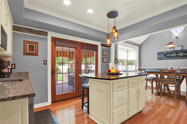 kitchen with light wood-type flooring, a sink, dark stone countertops, a kitchen bar, and pendant lighting
