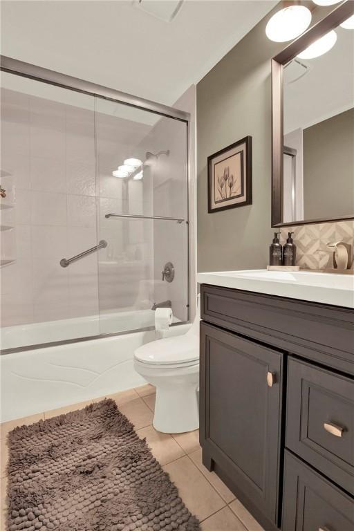 bathroom featuring tile patterned flooring, shower / bath combination with glass door, vanity, toilet, and backsplash