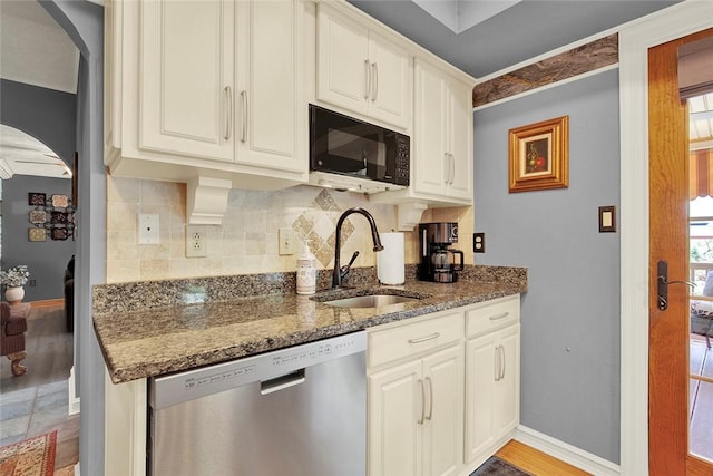 kitchen featuring dishwasher, black microwave, a sink, arched walkways, and dark stone counters