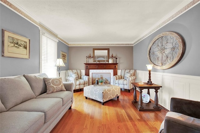 living area with wood finished floors, crown molding, and a wainscoted wall
