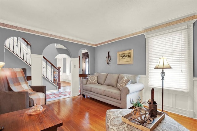living room with arched walkways, hardwood / wood-style floors, a wainscoted wall, stairs, and plenty of natural light