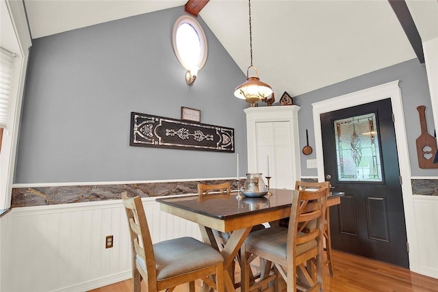 dining room with wainscoting, light wood-type flooring, and high vaulted ceiling