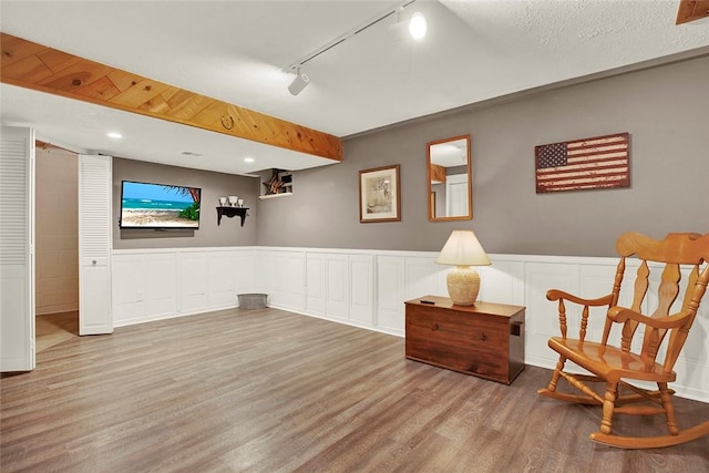 living area with wood finished floors, rail lighting, wainscoting, and a decorative wall