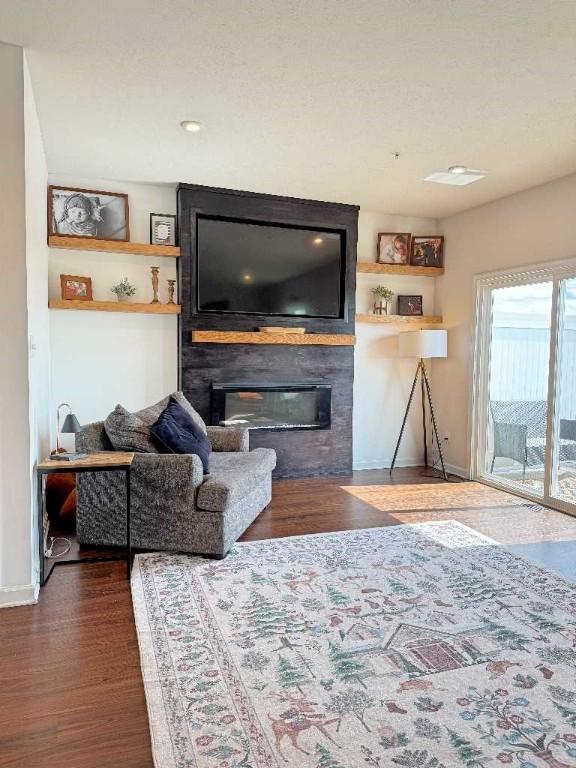 living room featuring a glass covered fireplace, wood finished floors, baseboards, and built in shelves