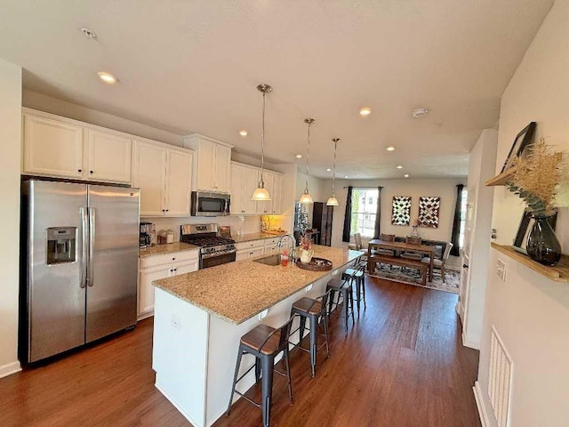 kitchen with stainless steel appliances, a sink, white cabinets, a kitchen breakfast bar, and a kitchen island with sink