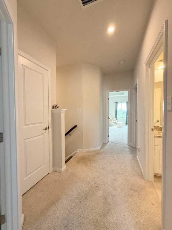 hallway with an upstairs landing, light colored carpet, baseboards, and recessed lighting