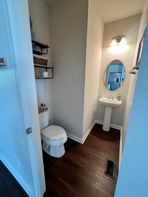 half bathroom with wood finished floors, toilet, and baseboards