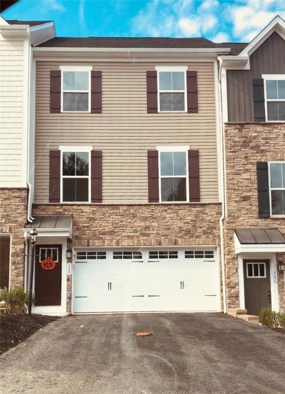 multi unit property with an attached garage, stone siding, and asphalt driveway