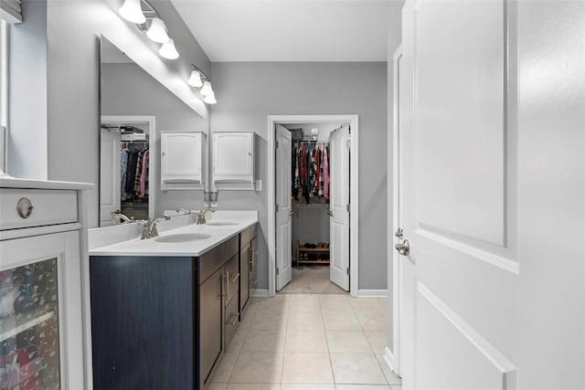 bathroom with double vanity, a spacious closet, tile patterned flooring, and baseboards